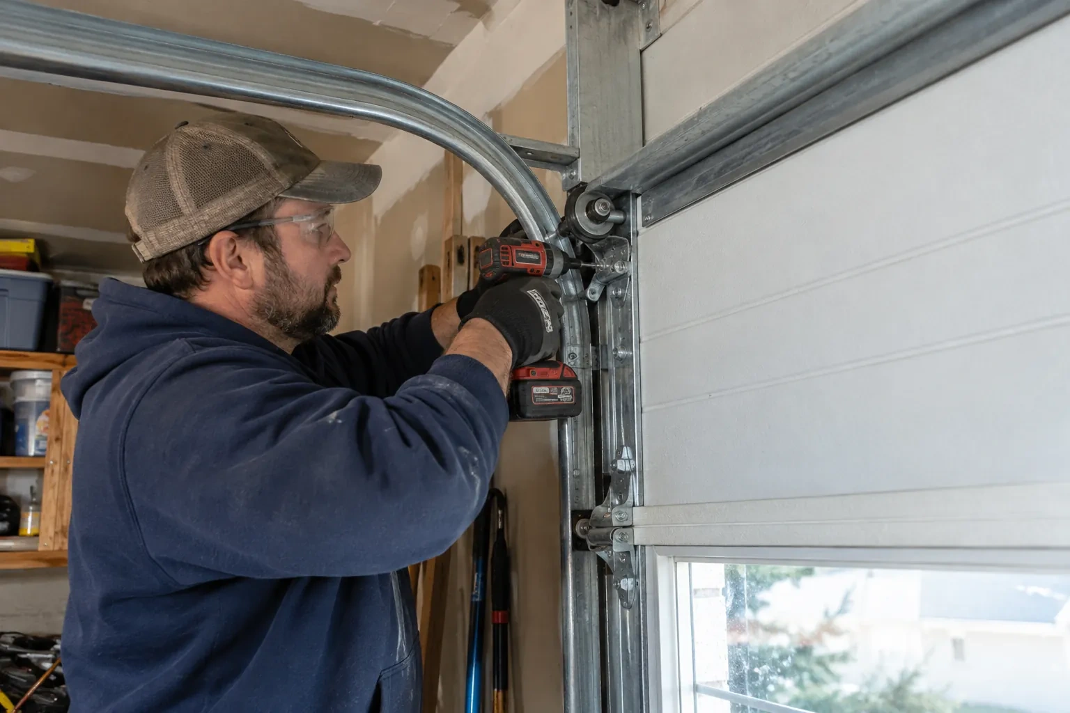 Technician in a mesh cap driving a screw with a cordless drill into a roller bracket beside a curved metal track. — Mount Pleasant